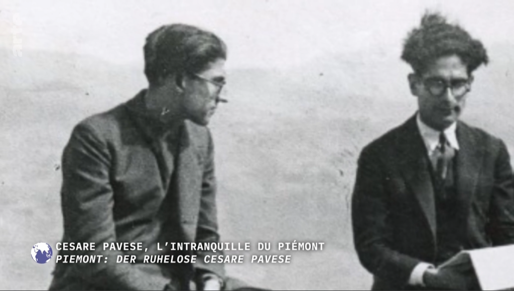 Fotogramma del film "Cesare Pavese, l'intranquille du Piémont". Nel fotogramma è ritratto Cesare Pavese con altri tre uomini, tutti seduti su un muretto con le spalle alle colline.